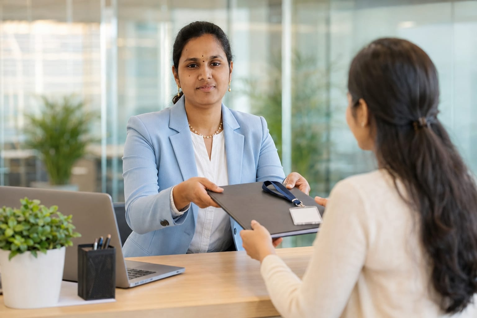 Vennela Nagilla handing over a document folder to a colleague in an office